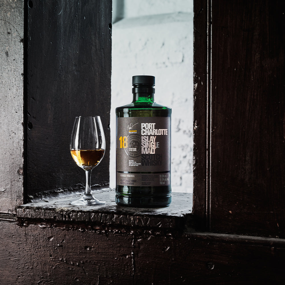 Port Charlotte 18 Islay single malt Scotch whisky bottle beside a glass of whisky on a dark wooden surface feature-row__image lazyloaded bottle from Bruichladdich Distillery