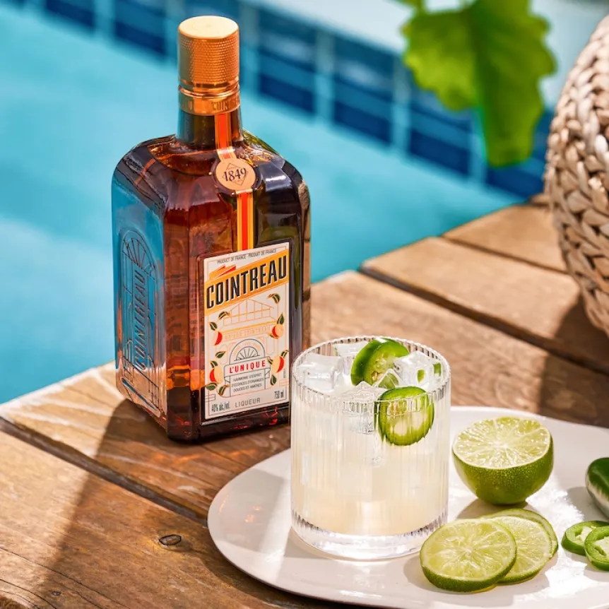 A Spicy Margarita in a short drinking glass with lime slices and beside a cut up lime on a white plate, positioning in front of a Cointreau bottle media__image media__element bottle from Carré Cointreau